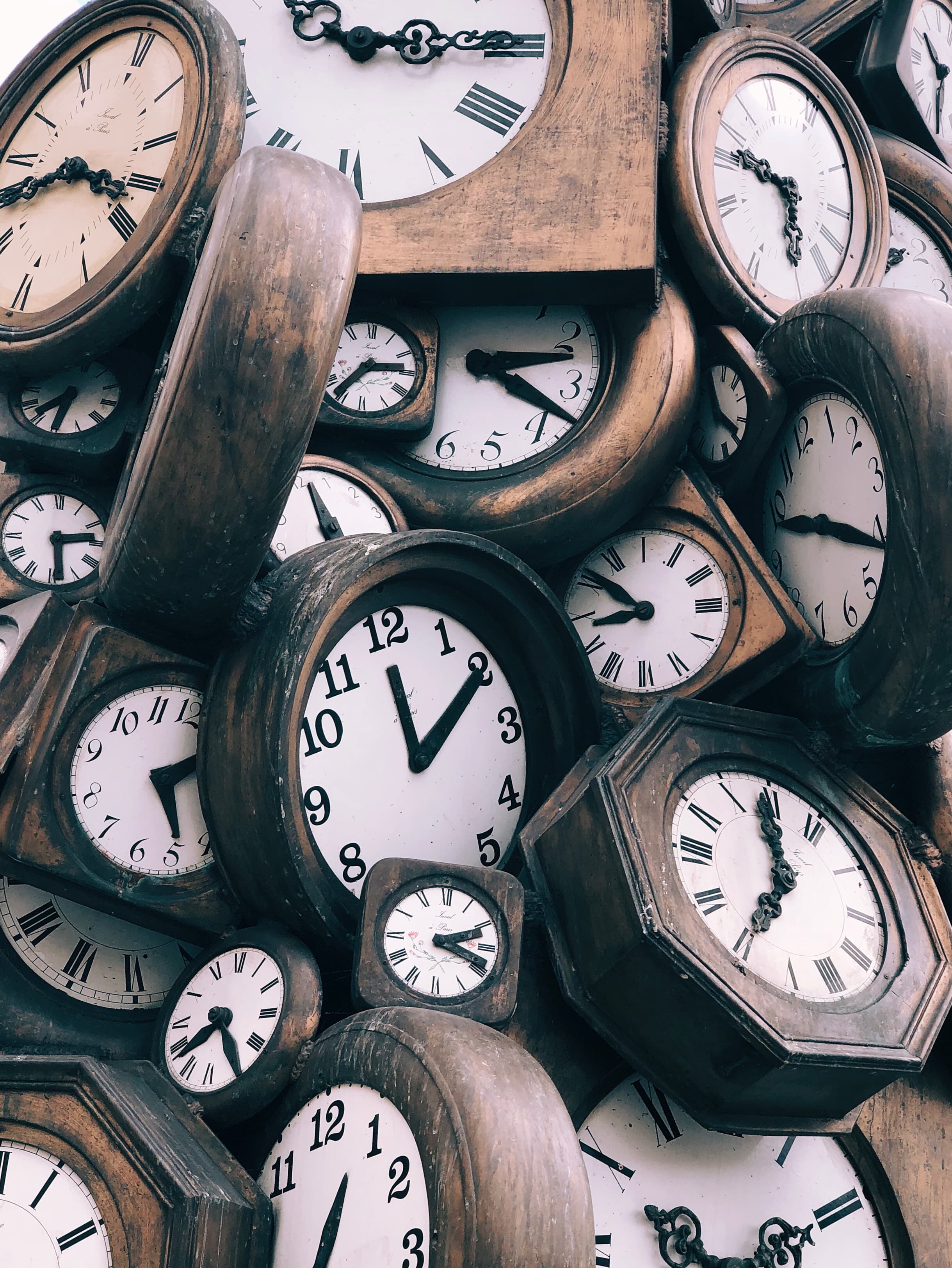 Multiple analog clocks of different sizes all in a pile. Each clock shows a different time.
