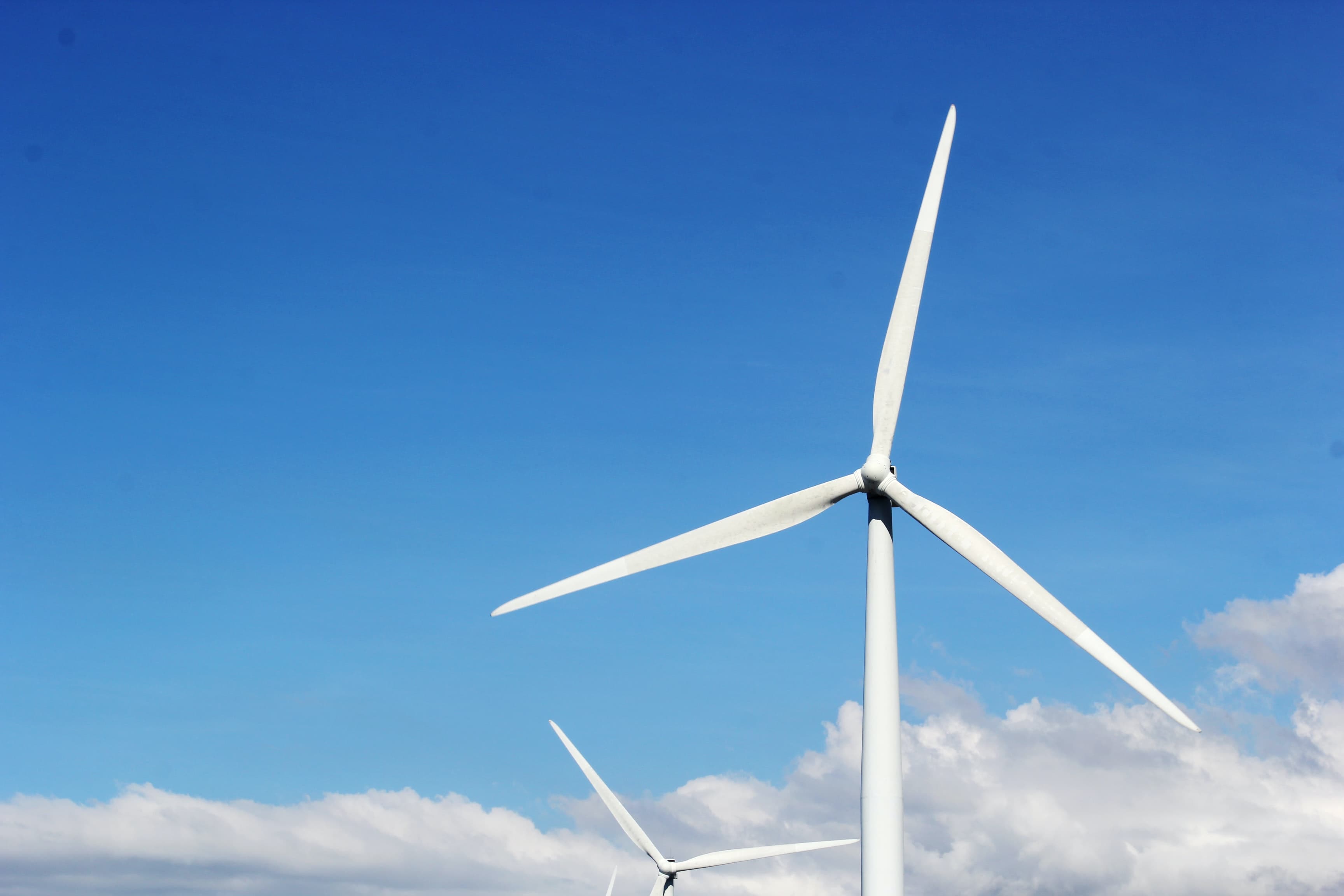 A white windmill with three blades against a clear blue sky.