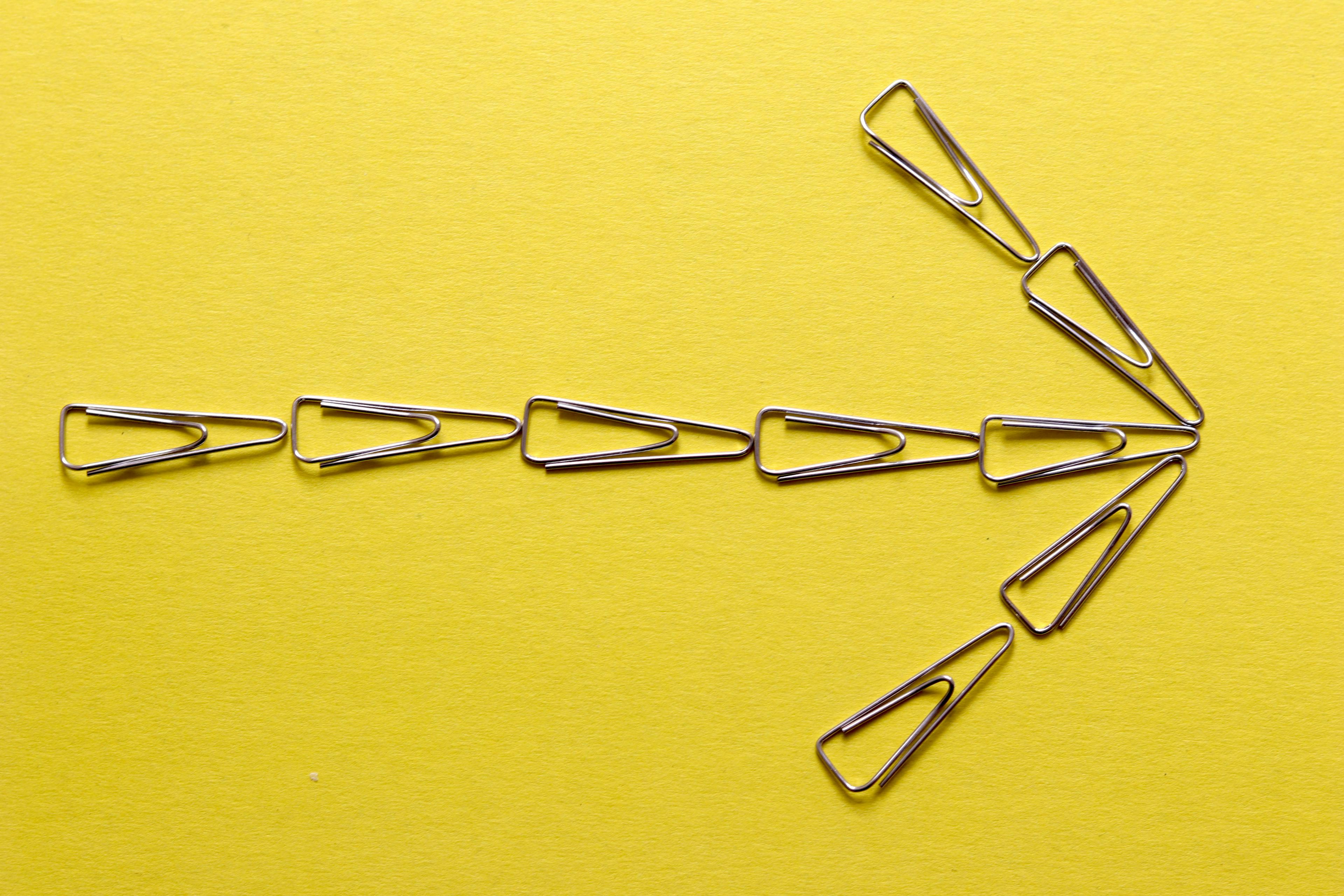 an arrow made of paper clips on a yellow background