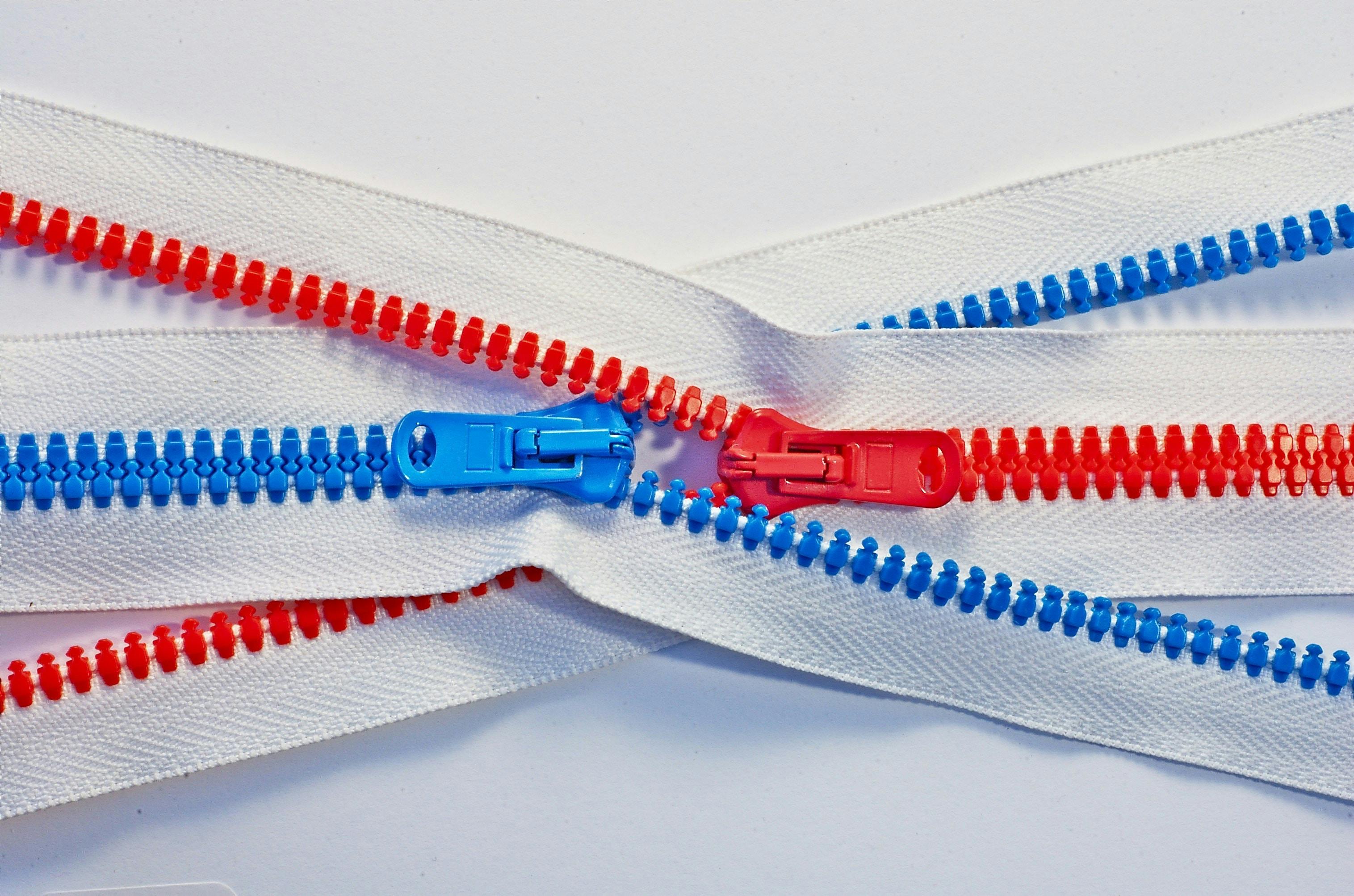 A red zipper and blue zipper interlocked and going in opposite directions.